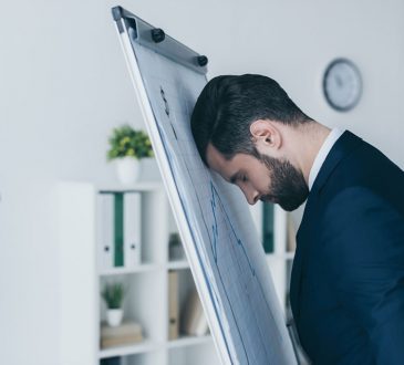 Depressed businessman standing with closed eyes and leaning at flipchart with forehead