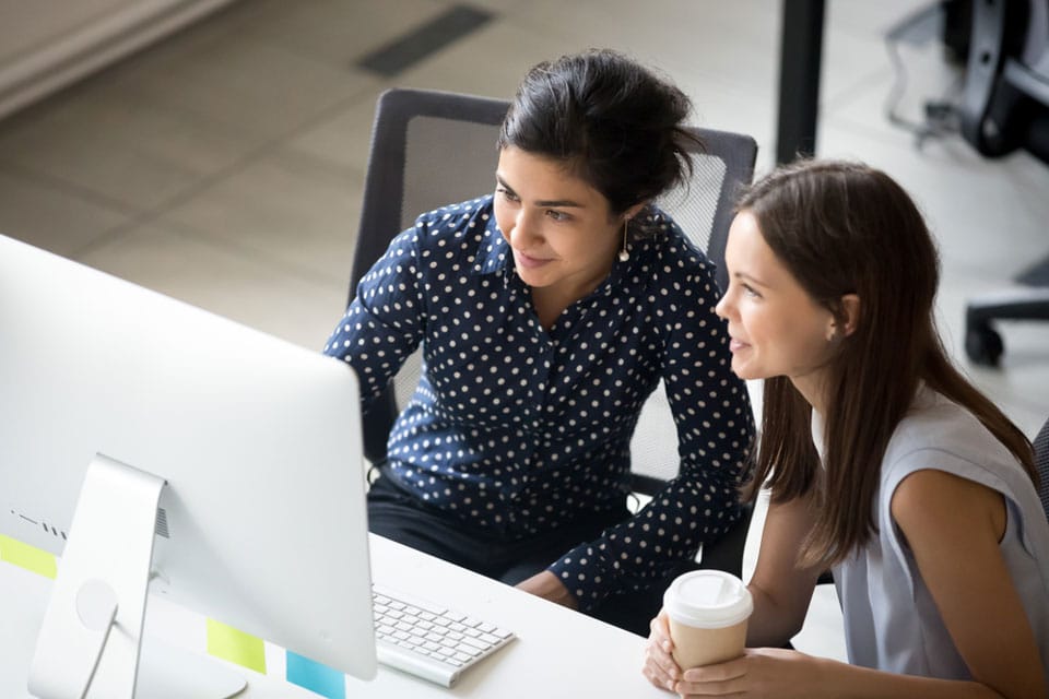 two women sitting at a table looking at a computer screen
