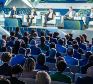 business conference with a panel of speakers and a diverse audience in attendance, focusing on various topics and discussions.