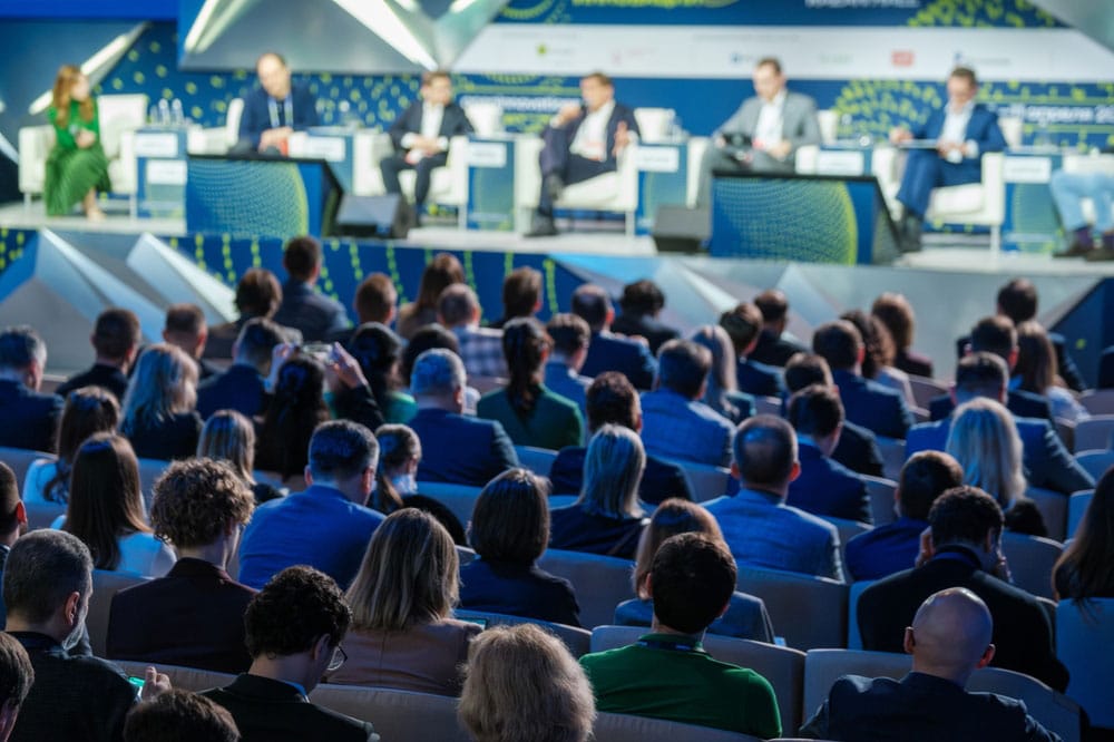 business conference with a panel of speakers and a diverse audience in attendance, focusing on various topics and discussions.