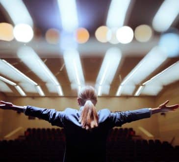 Happy Motivational Speaker Raising her Hands in Conference Hall Inspirational speaker making presentation with enthusiastic pathos