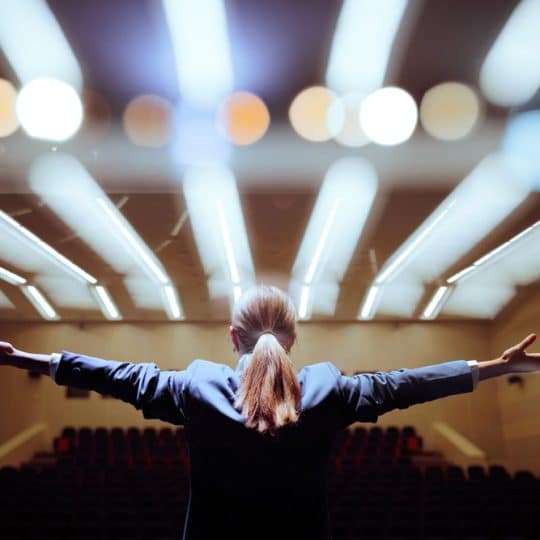 Happy Motivational Speaker Raising her Hands in Conference Hall Inspirational speaker making presentation with enthusiastic pathos