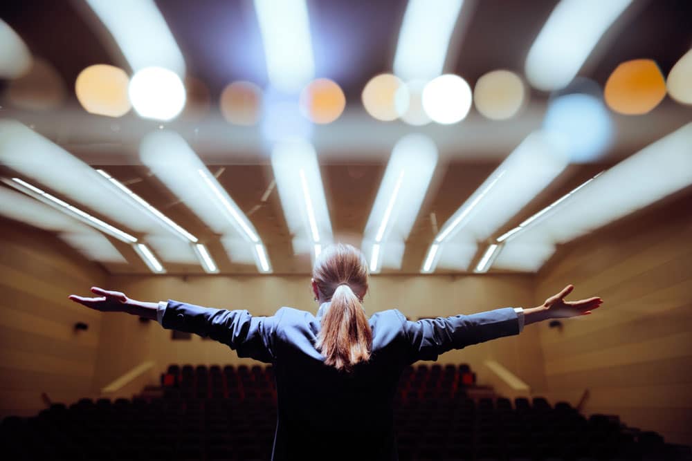 Happy Motivational Speaker Raising her Hands in Conference Hall Inspirational speaker making presentation with enthusiastic pathos